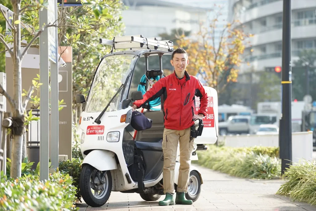 ハウスクリーニングスタッフが道具を積んだ作業用バイクの横に立っている写真