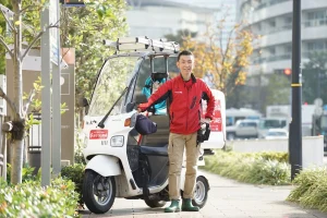 ハウスクリーニングスタッフが道具を積んだ作業用バイクの横に立っている写真