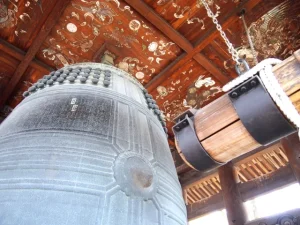 寺院の堂内に吊り下げられた大きな梵鐘を見上げて撮影した写真。天井には彩色された装飾が施されている