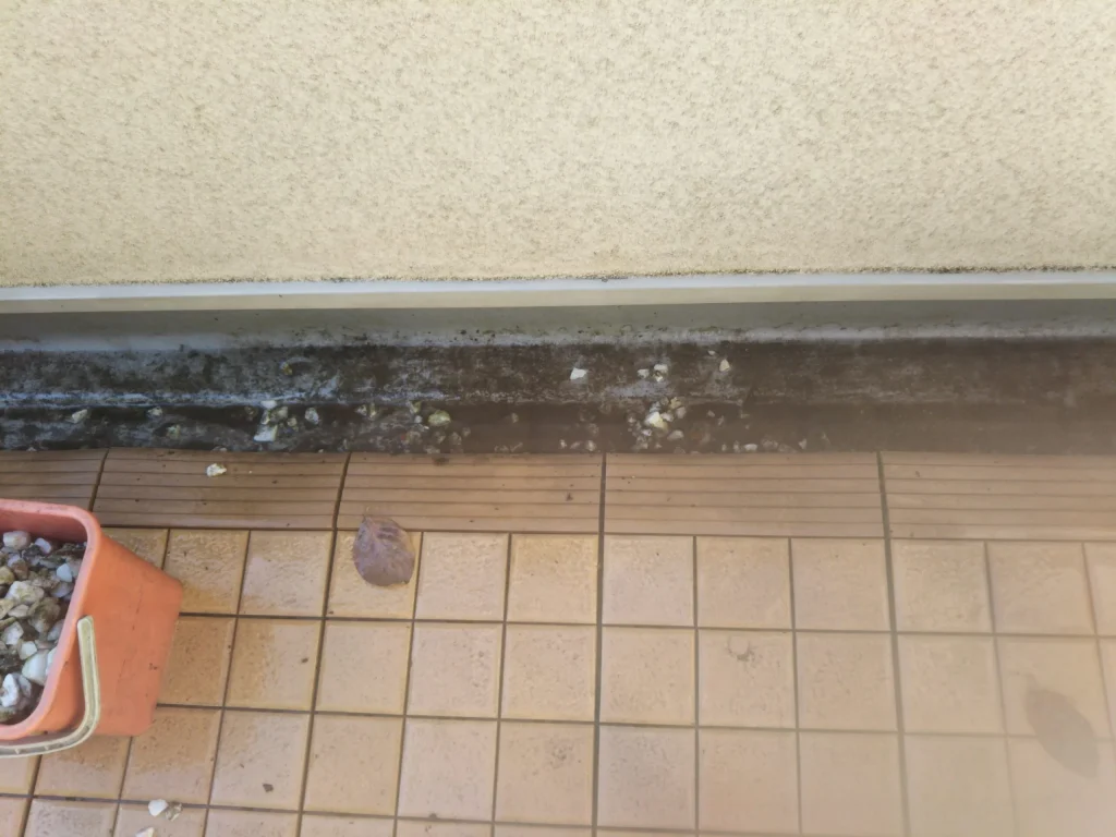 汚れの付着した窓のサッシレールとバケツが写った清掃前の写真