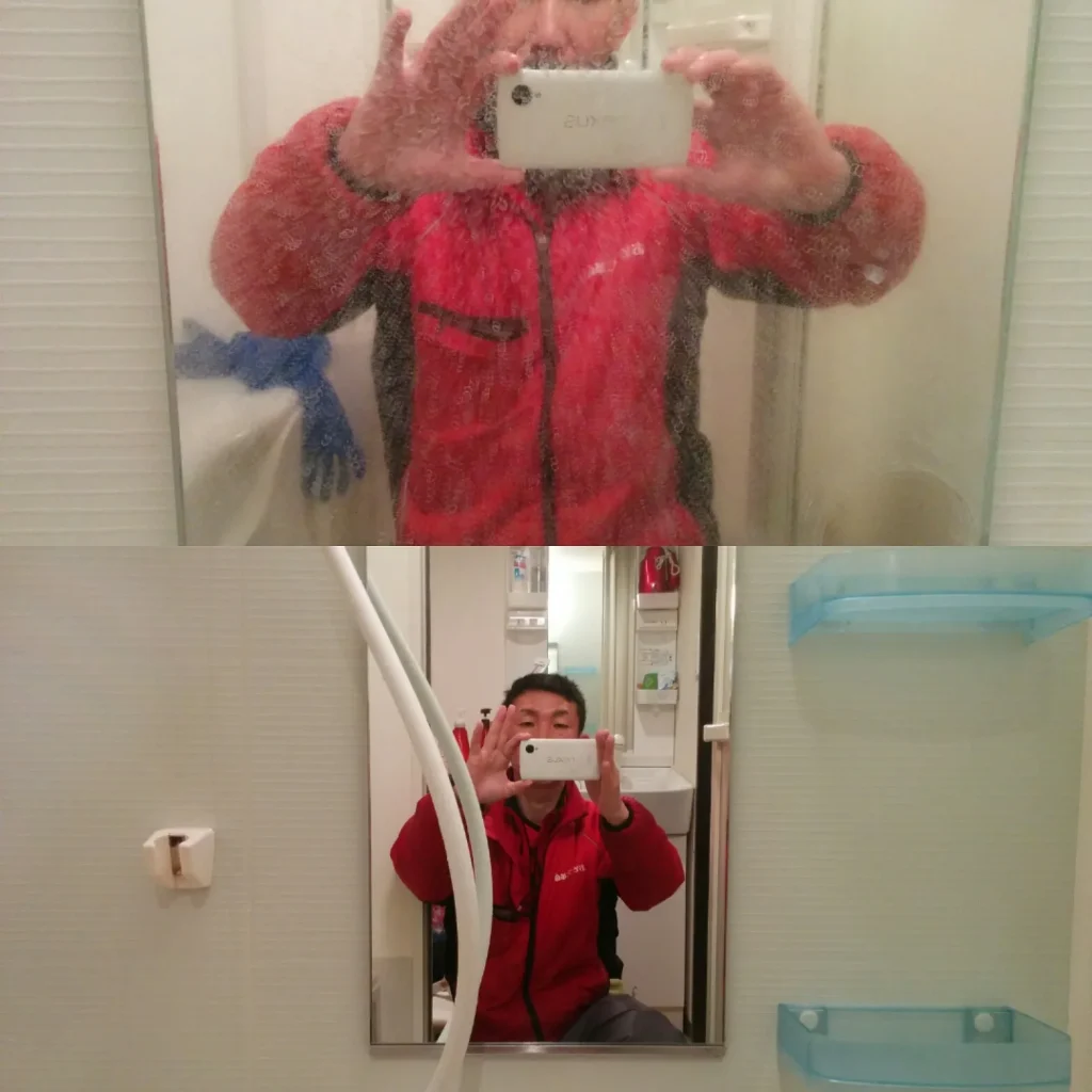 赤い作業用レインコートを着た作業スタッフが洗面所の鏡越しにスマートフォンで自撮りしている写真