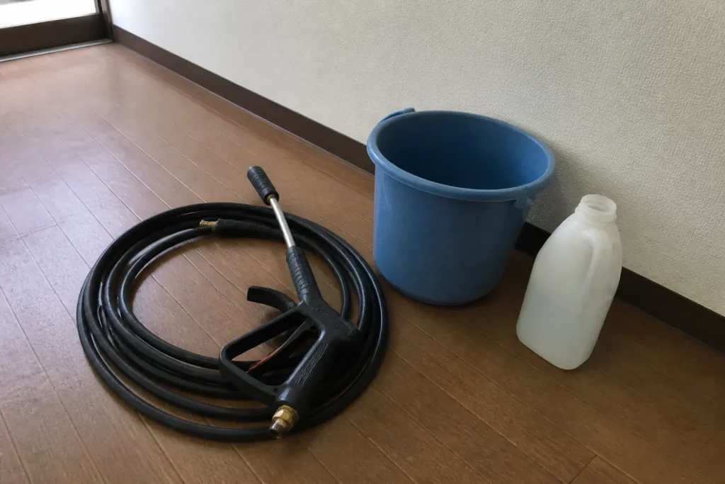 フローリングに並べた高圧洗浄用ホースとガン、青いバケツ、洗剤ボトル