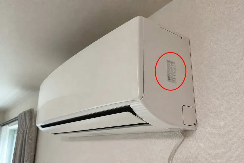 壁掛けエアコンの右側面にある品番シールの位置を赤い丸で示した案内写真