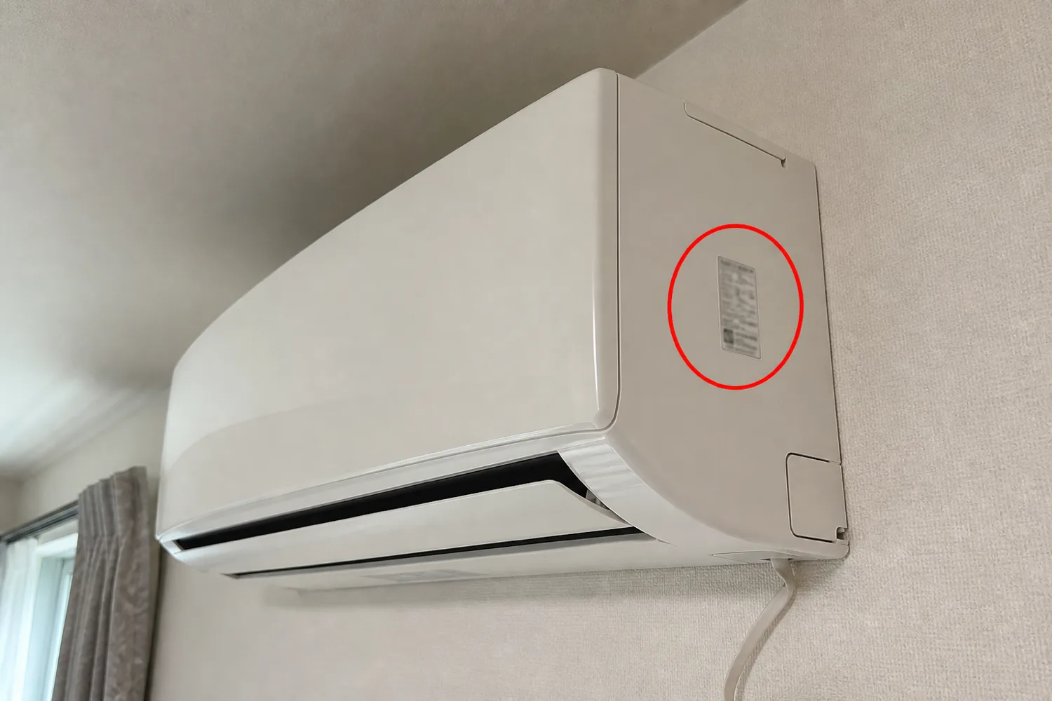 壁掛けエアコンの右側面にある品番シールの位置を赤い丸で示した案内写真