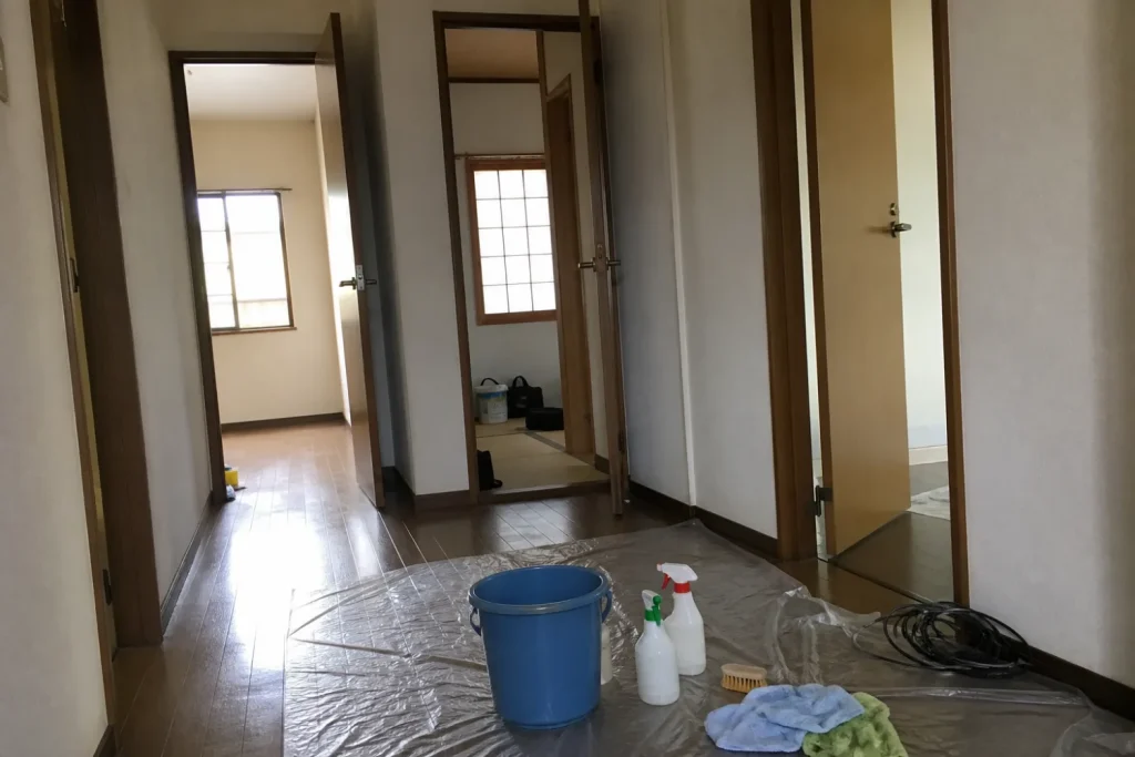 養生シートを敷いた廊下にバケツとスプレーを置き、複数の部屋のドアが開いている作業中の様子